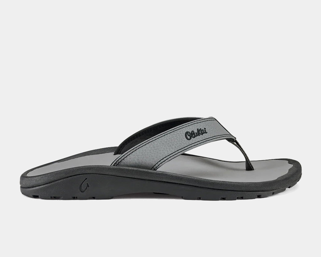 A pair of grey Ohana sandals by Olukai, featuring a water-resistant synthetic strap and a non-marking rubber outsole with a coral reef lug design.