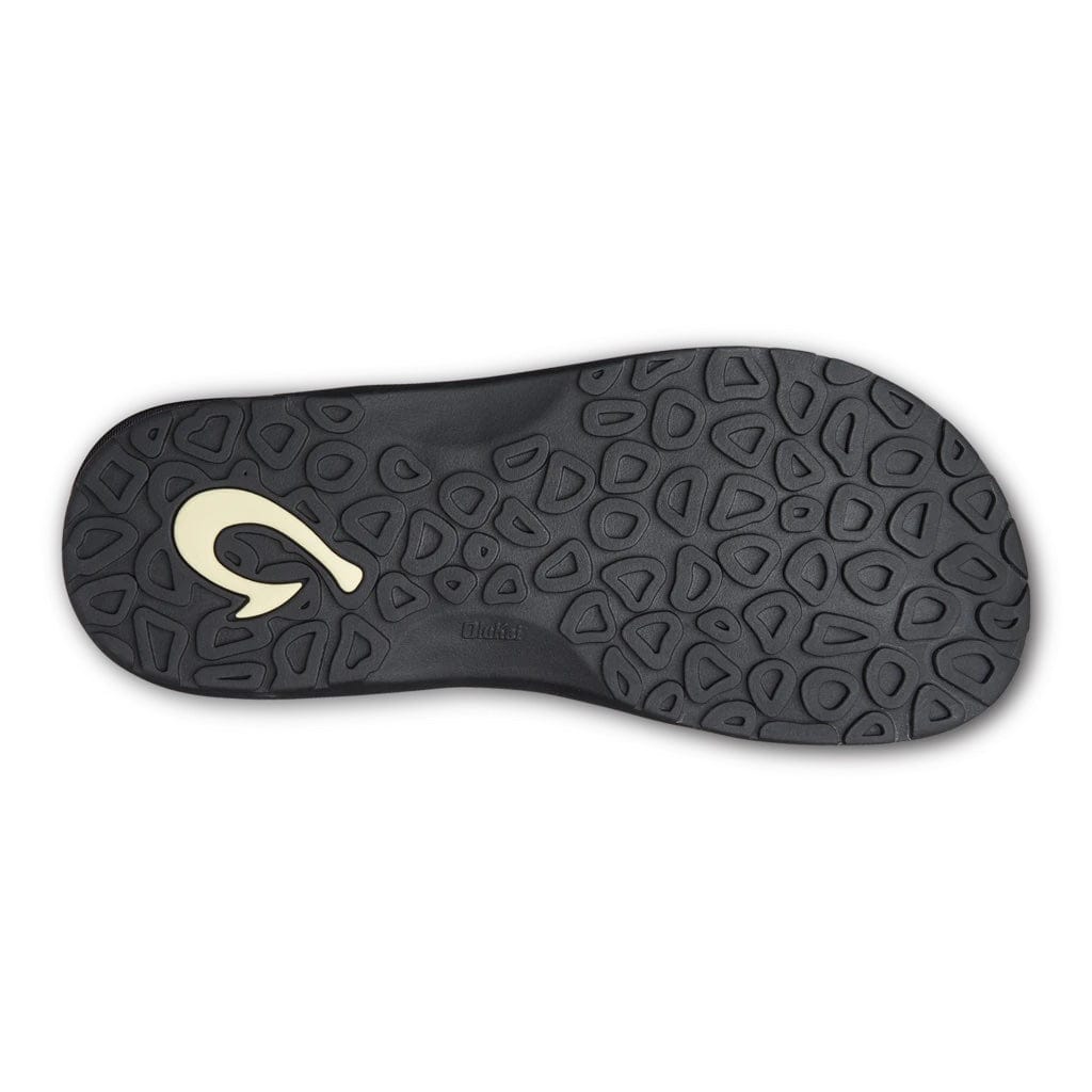 OluKai Ohana sandal outsole in black rubber with textured traction pattern and beige logo detail, bottom view.