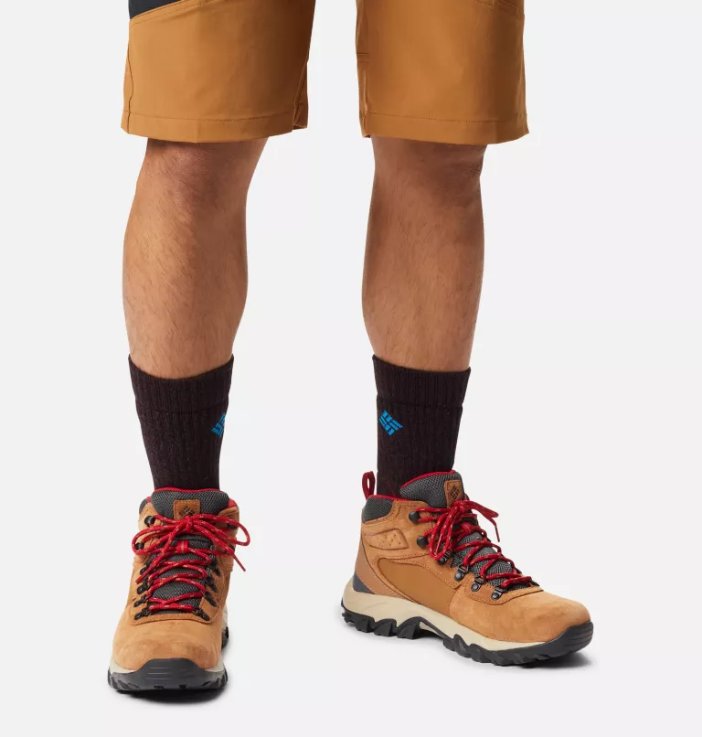 Columbia Newton Ridge Plus II Suede WP hiking boots in light brown suede with red laces and black outsole, worn by a person outdoors.