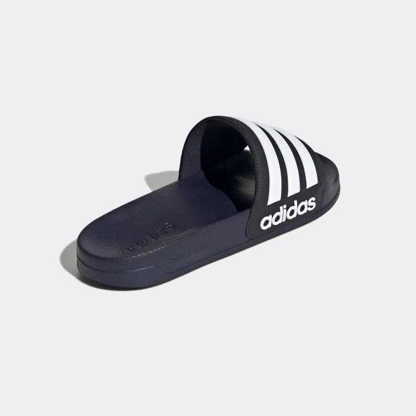 Adidas Adilette Shower Slides in navy blue with white stripes and logo, contoured footbed and synthetic upper, side angle.