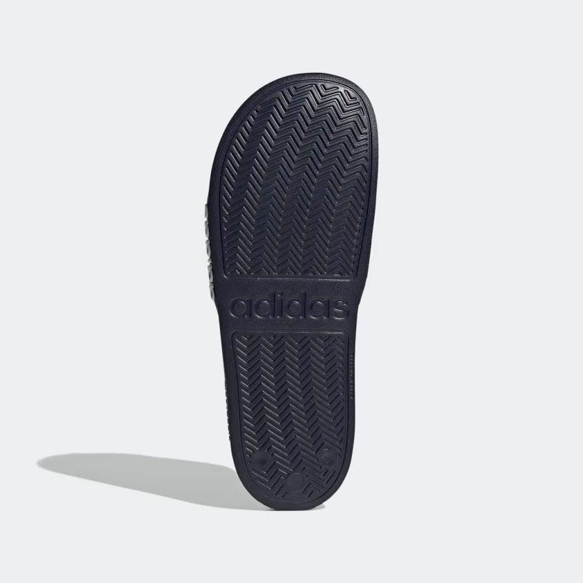 Adidas Adilette Shower Slides outsole with textured herringbone pattern in navy blue, bottom view showing brand logo detailing.