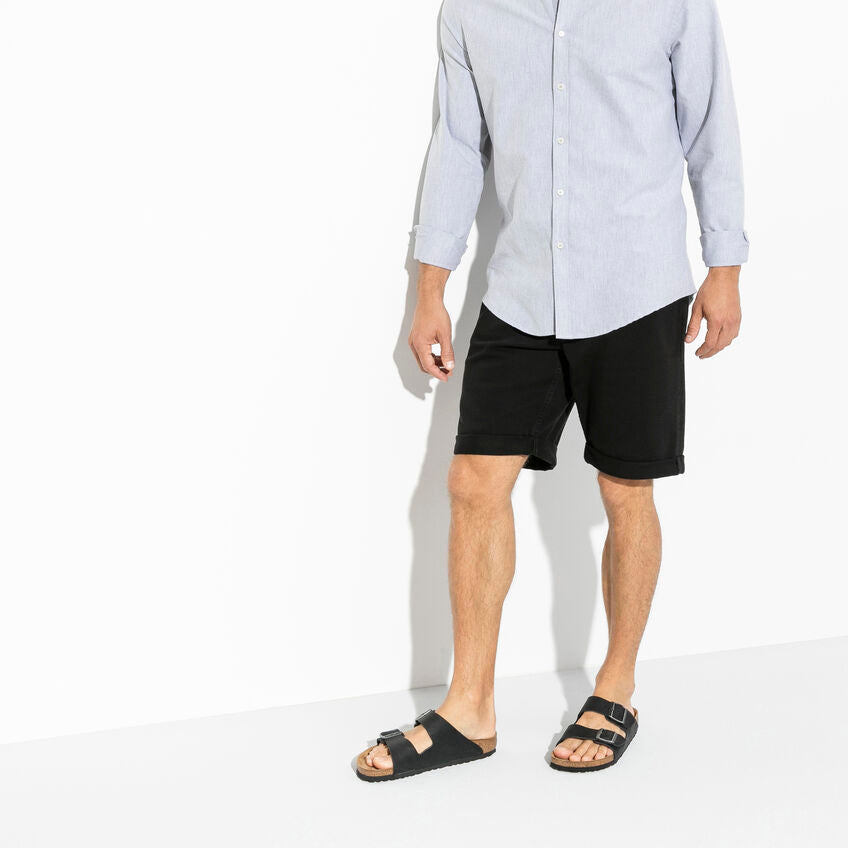 Birkenstock Arizona Oiled Leather sandals in black with dual adjustable buckle straps and cork footbed, worn by man standing.