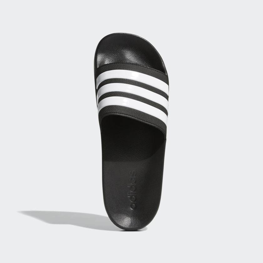 Adidas Adilette Shower Slides in black with white three-stripe design, top view showing contoured footbed and branding.