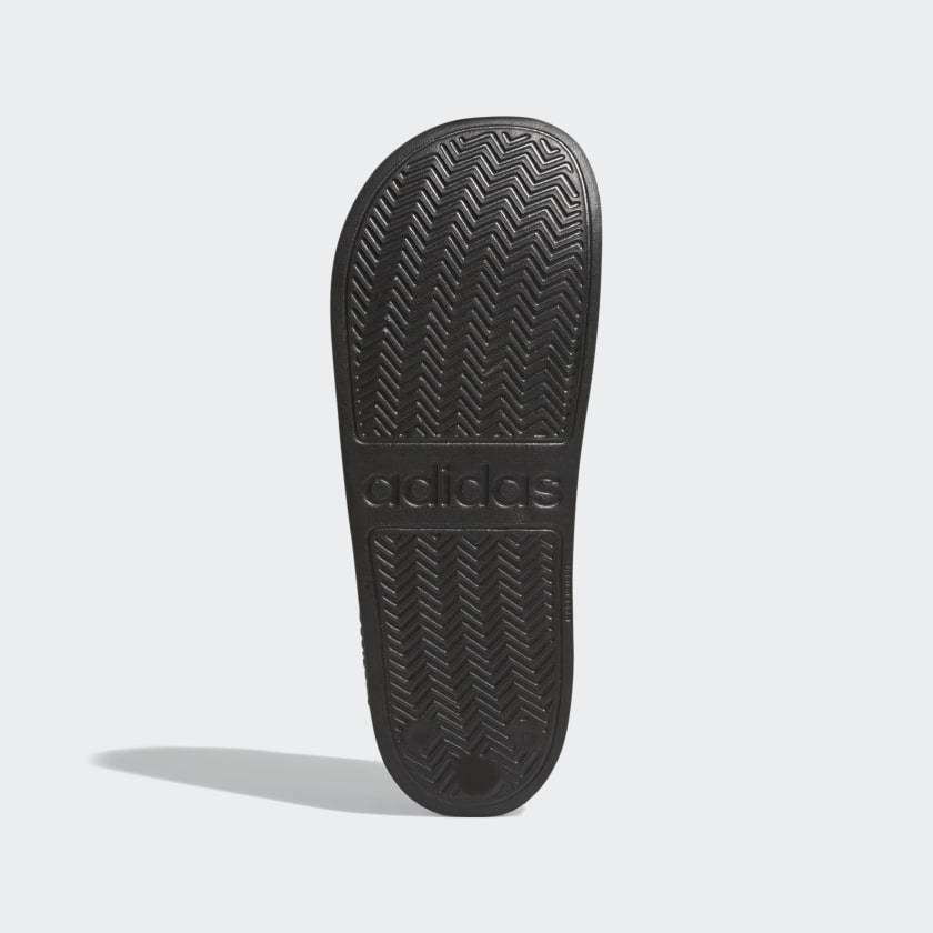 Adidas Adilette Shower Slides outsole in black showing chevron traction pattern and embossed logo, sole/bottom view.