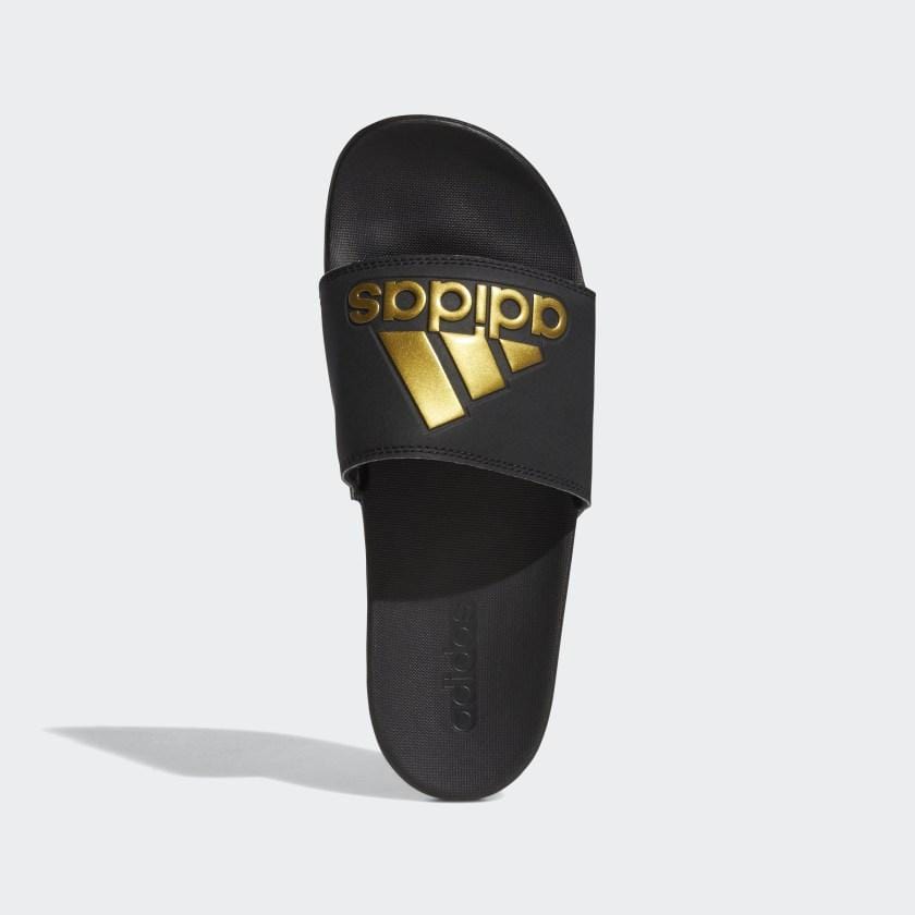 Adidas Adilette Comfort Slides in black with gold logo detailing and contoured footbed, top view.
