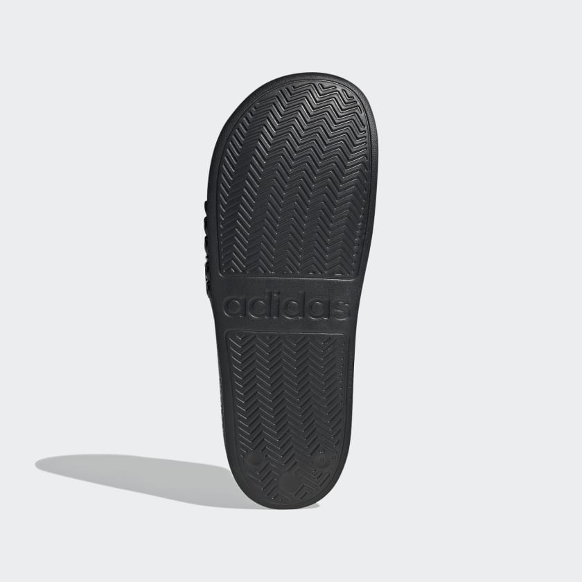 Adidas Adilette Shower Slides outsole in black showing textured herringbone traction pattern and embossed logo, sole/bottom view.