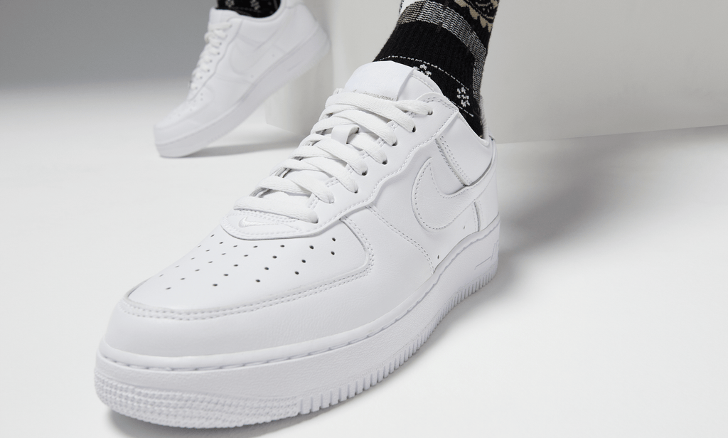 Nike Air Force 1 '07 sneakers in white leather with perforated toe box and signature Swoosh logo, angled front view worn casually.