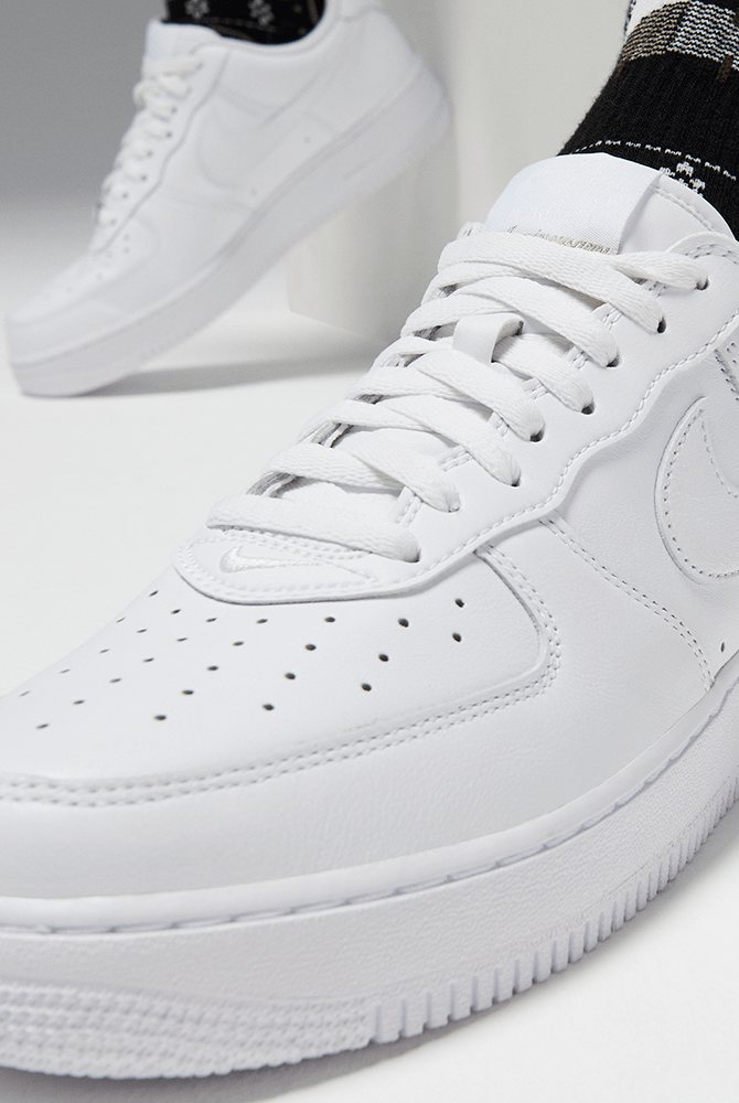 Nike Air Force 1 '07 sneakers in all-white leather with perforated toe box and iconic Swoosh logo, side view close-up.