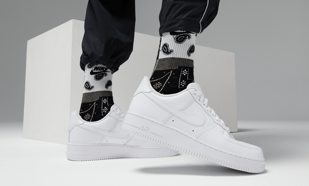 Nike Air Force 1 '07 shoes in classic white leather with tonal stitching and perforated toe box, lifestyle view worn with socks.