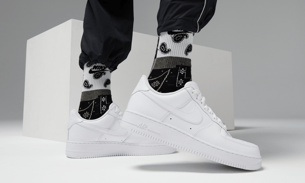 Nike Air Force 1 '07 shoes in classic white leather with tonal stitching and perforated toe box, lifestyle view worn with socks.