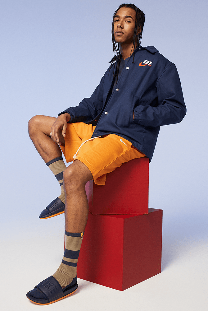 Nike Offcourt Slide sandals in navy blue with bold embossed branding and orange soles, worn with striped socks.