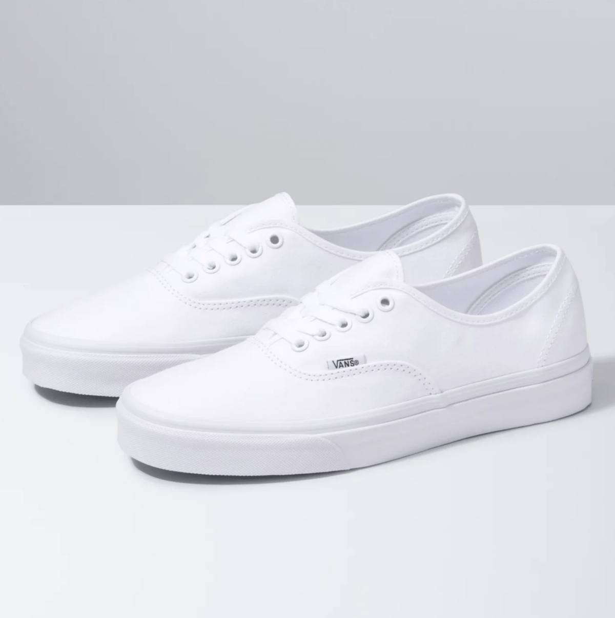 Vans Authentic sneakers in solid white with canvas upper, metal eyelets, and rubber outsole, angled front-side view.