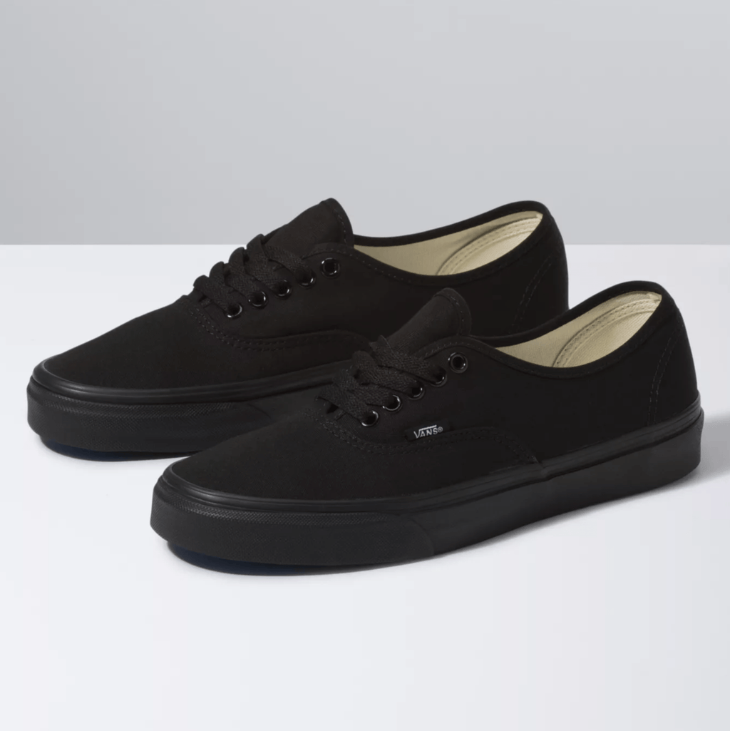 Vans Authentic sneakers in black canvas with black metal eyelets and matching black rubber soles, angled front-side view.