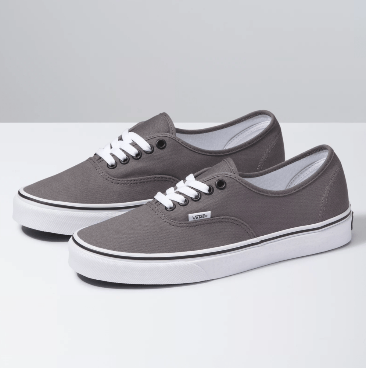 Vans Authentic sneakers in gray with canvas upper, white laces, metal eyelets, and vulcanized rubber outsole, angled side view.