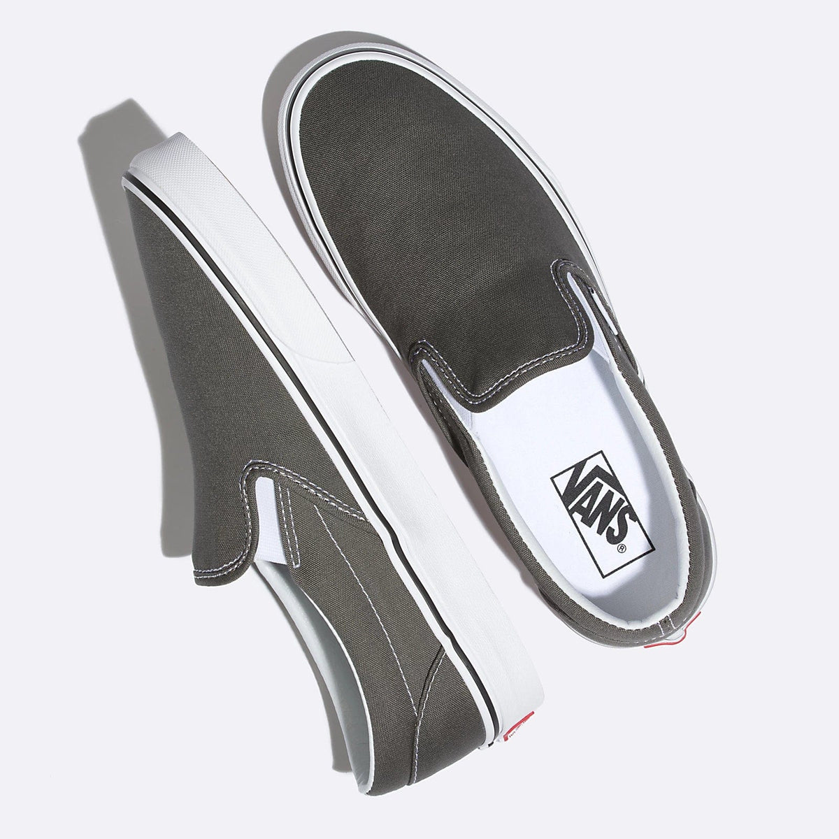 Vans Classic Slip On shoes in dark gray canvas with white stitching, padded collar, and white rubber midsole, top angled view.