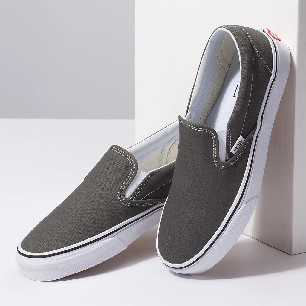 Vans Classic Slip On shoes in dark gray canvas with white rubber sole and elastic side accents, angled pair view.