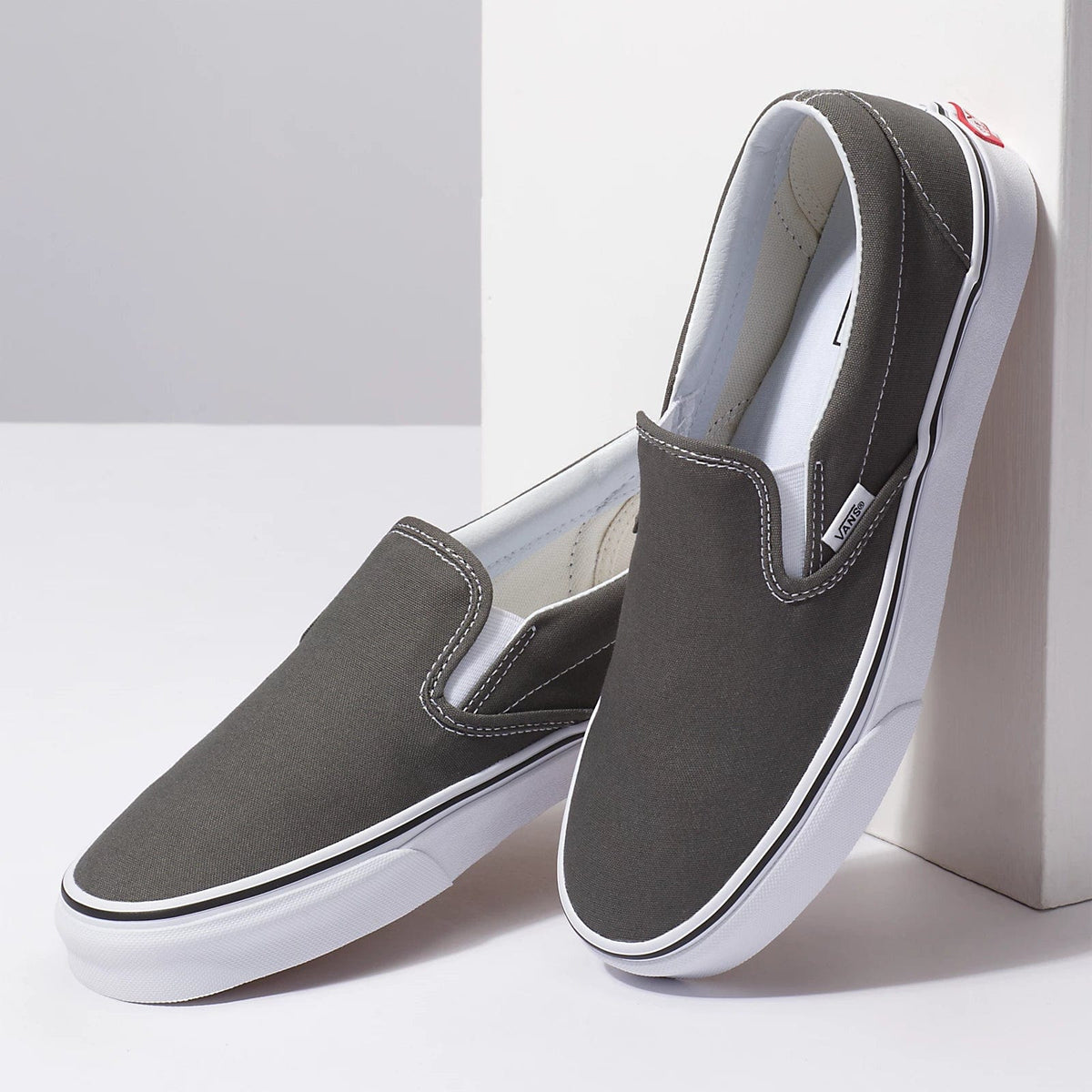Vans Classic Slip On shoes in dark gray canvas with white rubber sole and elastic side accents, angled pair view.
