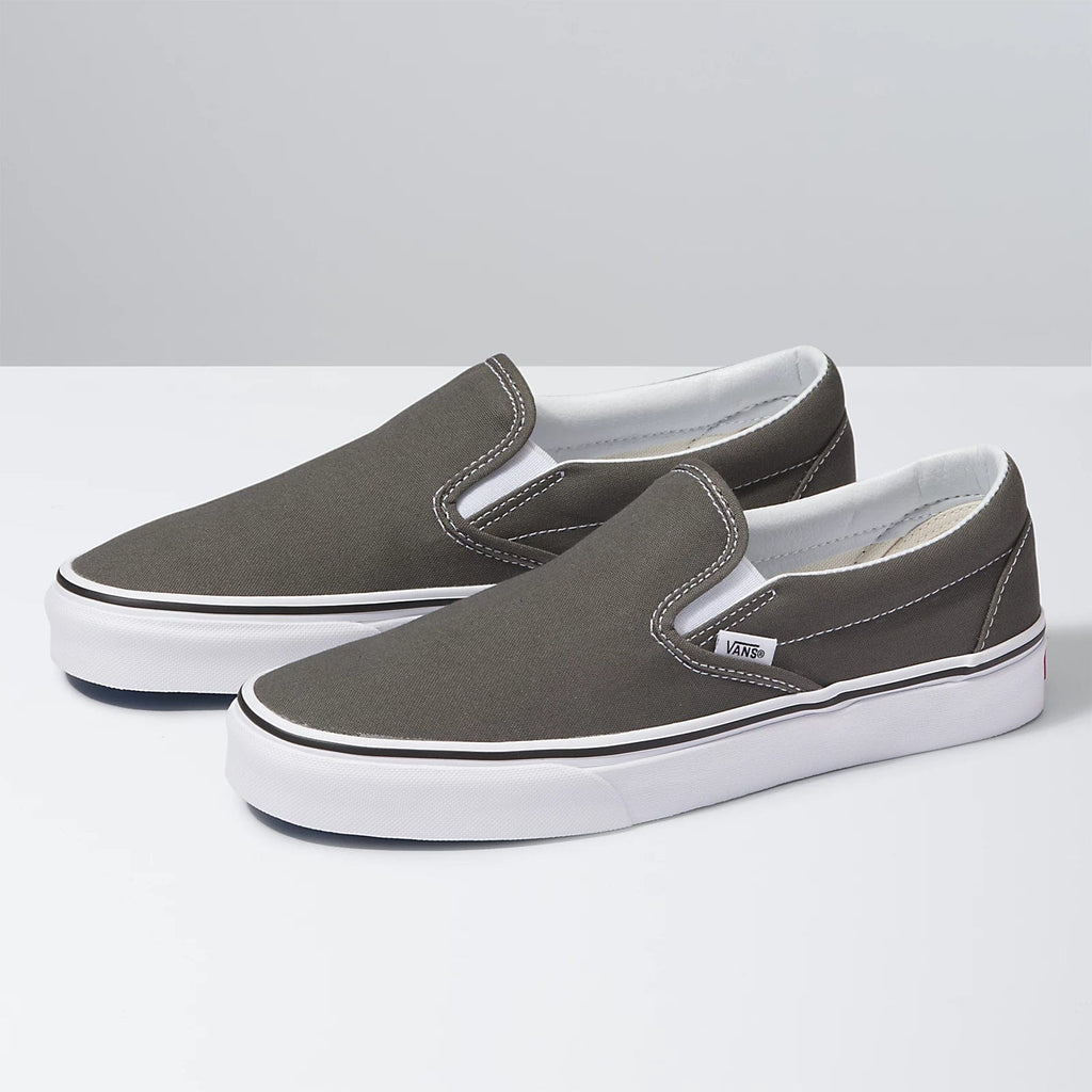 Vans Classic Slip On shoes in gray canvas with white stitching and rubber outsole, angled side view.