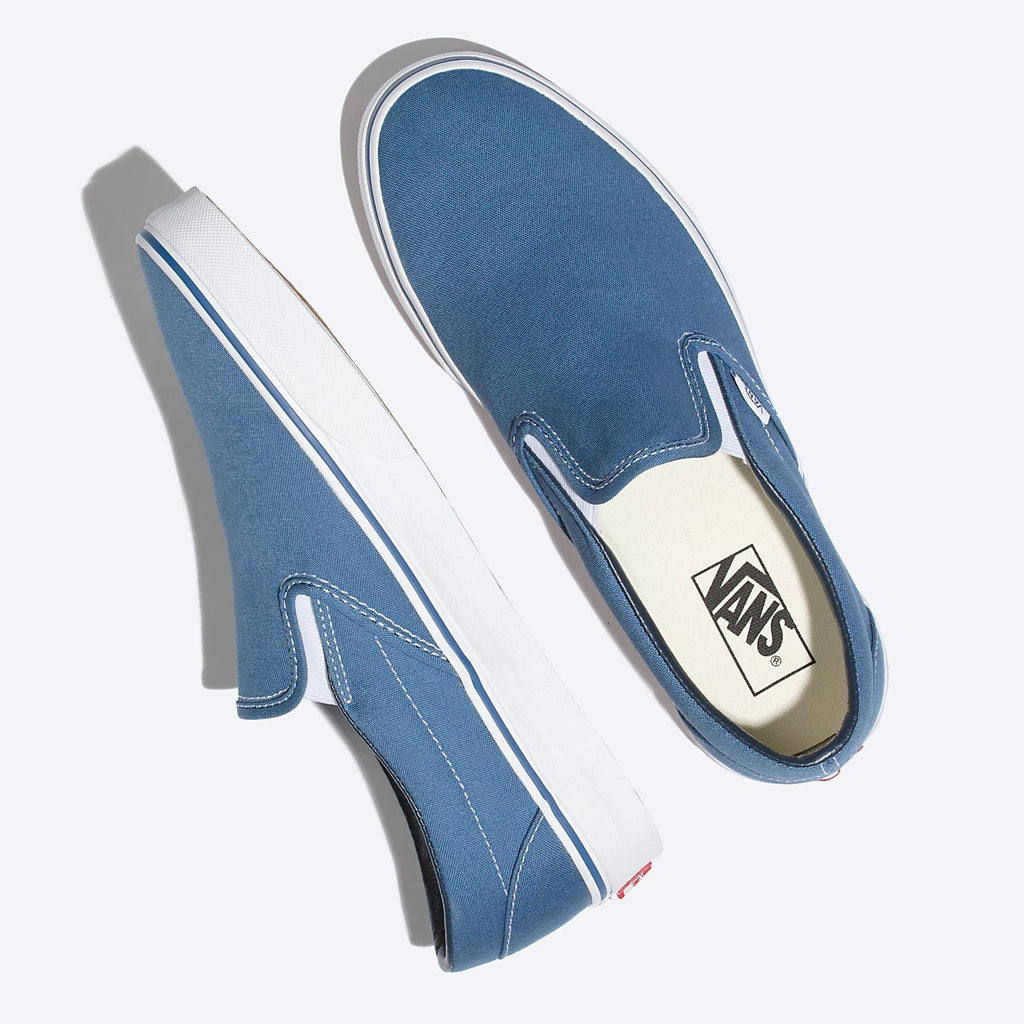 Vans Classic Slip On shoes in blue canvas with white rubber soles and elastic gore panels, top view.