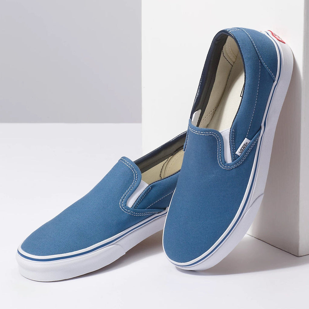 Vans Classic Slip On shoes in blue canvas with white rubber sole and elastic side accents, angled side view.