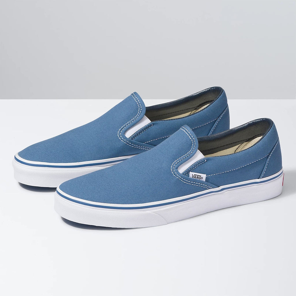 Vans Classic Slip On shoes in blue canvas with white midsoles and elastic side accents, angled side view.