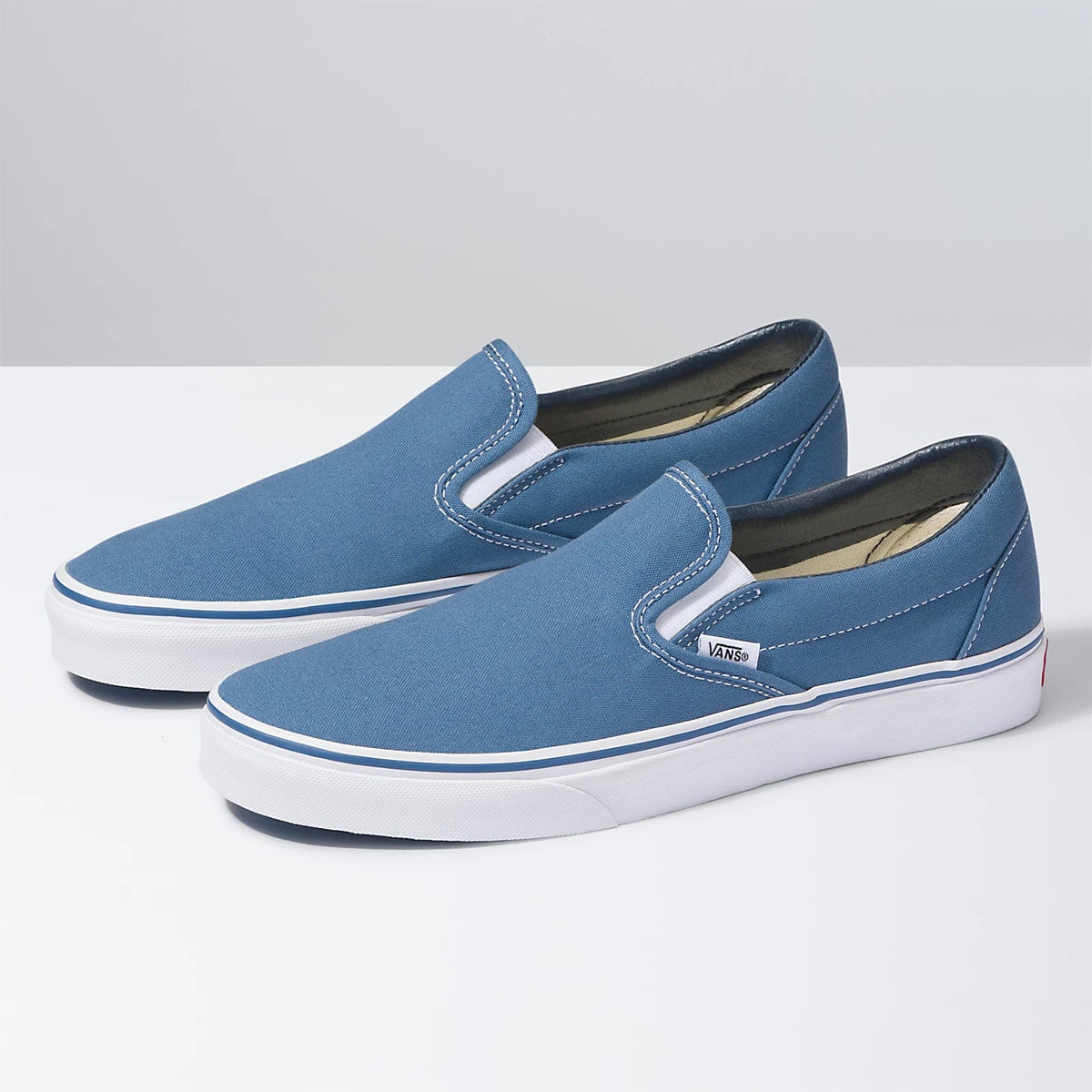 Vans Classic Slip On shoes in blue canvas with white midsoles and elastic side accents, angled side view.