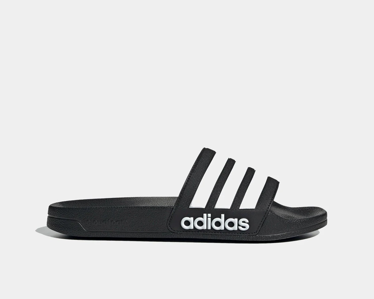 Adidas Adilette Shower Slides in black with white logo, synthetic strap and textured footbed, side profile view.