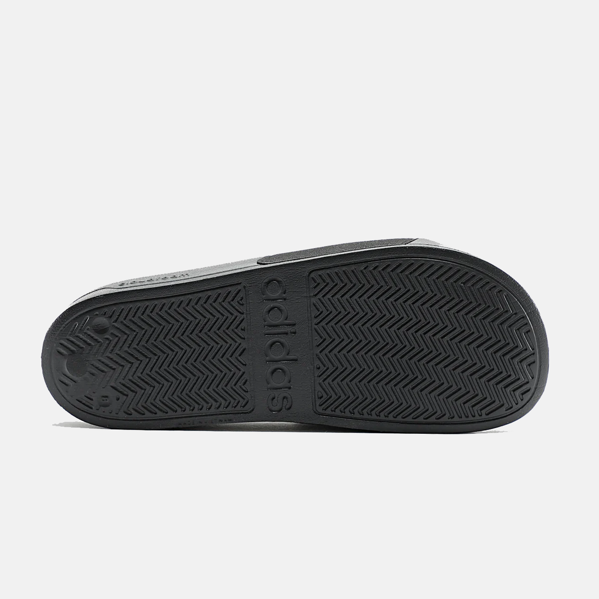 Adidas Adilette Shower Slides outsole in black rubber with textured grip pattern and embossed branding, bottom view