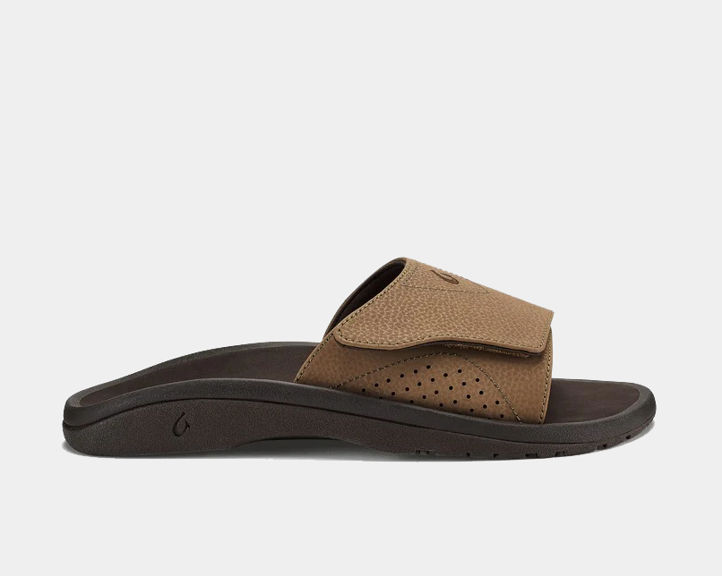 OluKai Nalu Slide sandals with adjustable brown leather strap, perforated details, and cushioned dark brown sole, side view.